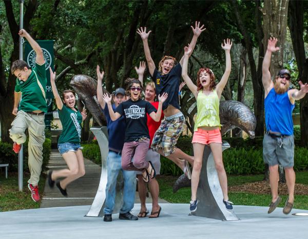 Students jumping in excitement after installing an iconic metal dolphin sculpture on campus.