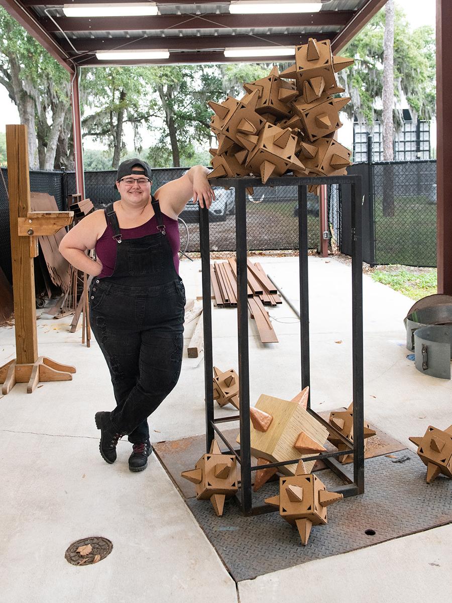 Student standing within the sculpture workshop fabricating and placing pieces of her work.
